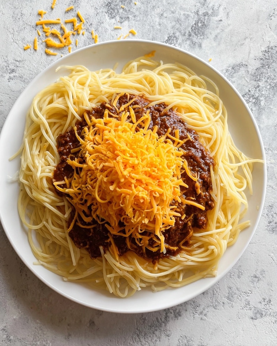 A white plate holds a dish with three clear layers: the bottom is long, pale yellow spaghetti noodles arranged loosely across the plate, the middle layer is thick, dark brown meat sauce spread over the center of the noodles, and the top layer is a bright orange pile of shredded cheddar cheese sitting in the middle of the sauce. Some stray strands of cheese are scattered on the white marbled surface around the plate. Photo taken with an iphone --ar 4:5 --v 7