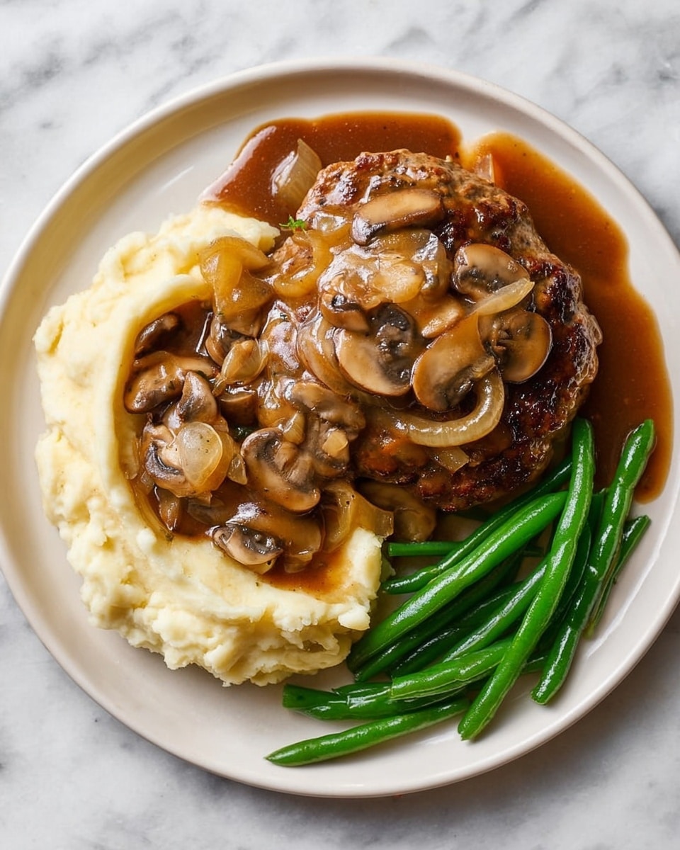 A white plate on a white marbled surface holds a serving of three main layers. At the bottom left is a creamy, off-white mashed potato layer with a smooth, fluffy texture. On top and slightly to the right is a round, golden-brown hamburger steak with a slightly charred and glossy surface. The steak is covered with a rich, dark brown mushroom gravy that includes visible sliced mushrooms and translucent onion rings evenly spread. At the bottom right are bright green, glossy steamed green beans, some slightly covered with the mushroom gravy. Photo taken with an iphone --ar 4:5 --v 7