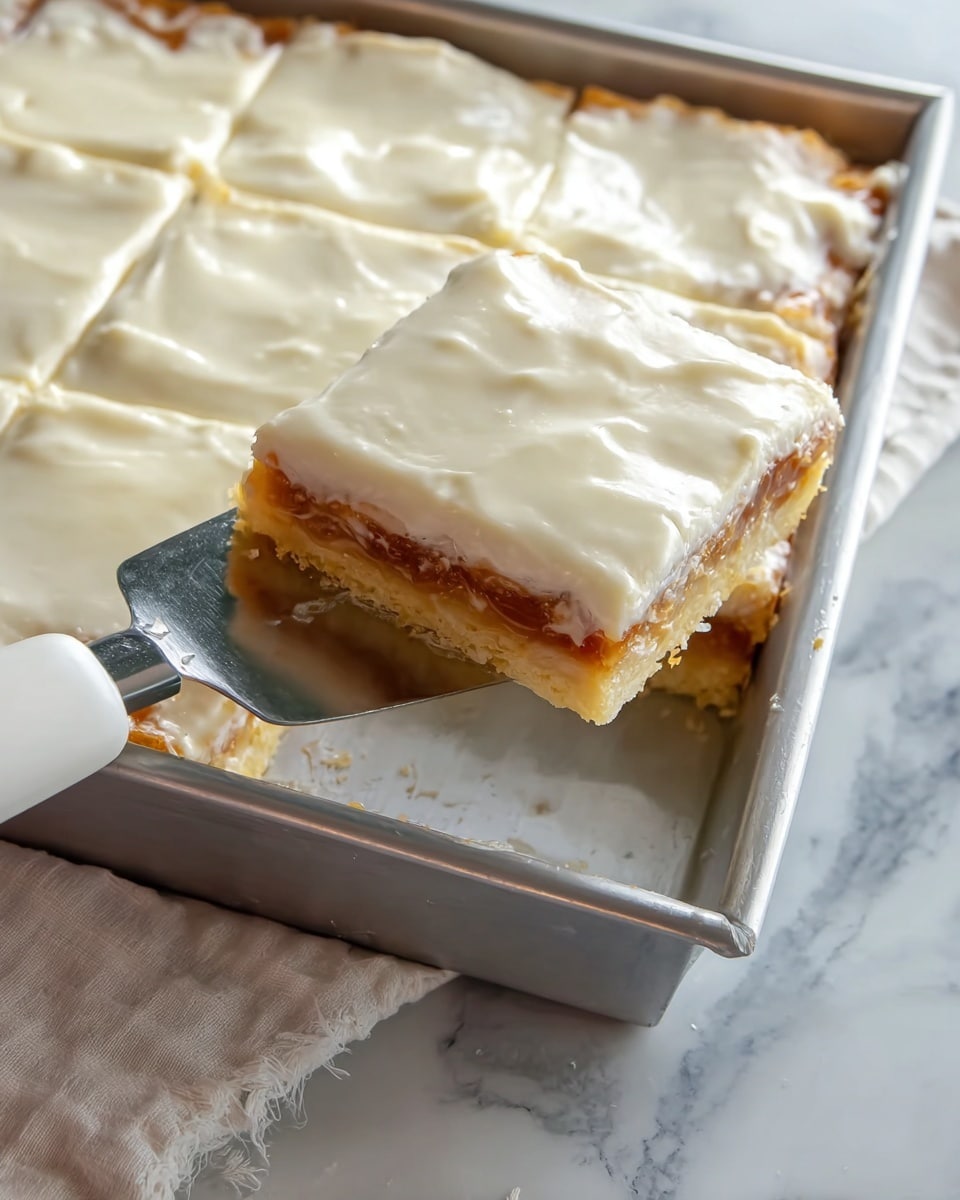 A close-up view of a square pastry with three visible layers: a golden-brown flaky crust at the bottom, a thin layer of light brown filling in the middle, and a thick, smooth, creamy white icing layer on top. One square piece is being lifted with a shiny metal spatula that has a white handle, revealing the same three layers clearly. The pastry sits in a metal baking pan placed on a white marbled surface with a light-colored cloth partially visible nearby. The icing has a slightly glossy texture with a few uneven bumps. Photo taken with an iphone --ar 4:5 --v 7