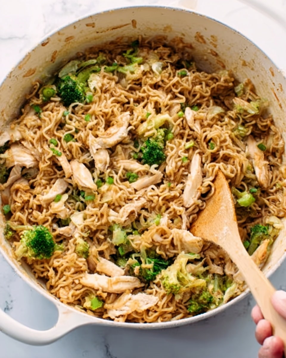 A white pot filled with a mix of cooked ramen noodles, shredded chicken, and small pieces of broccoli. The noodles are brown and look soft, covering most of the pot. The chicken pieces are white and scattered evenly among the noodles. Bright green broccoli bits add color and texture on top and throughout the dish. A wooden spatula is stirring the food, held by a woman's hand visible on the right edge of the pot. The pot sits on a white marbled surface. photo taken with an iphone --ar 4:5 --v 7