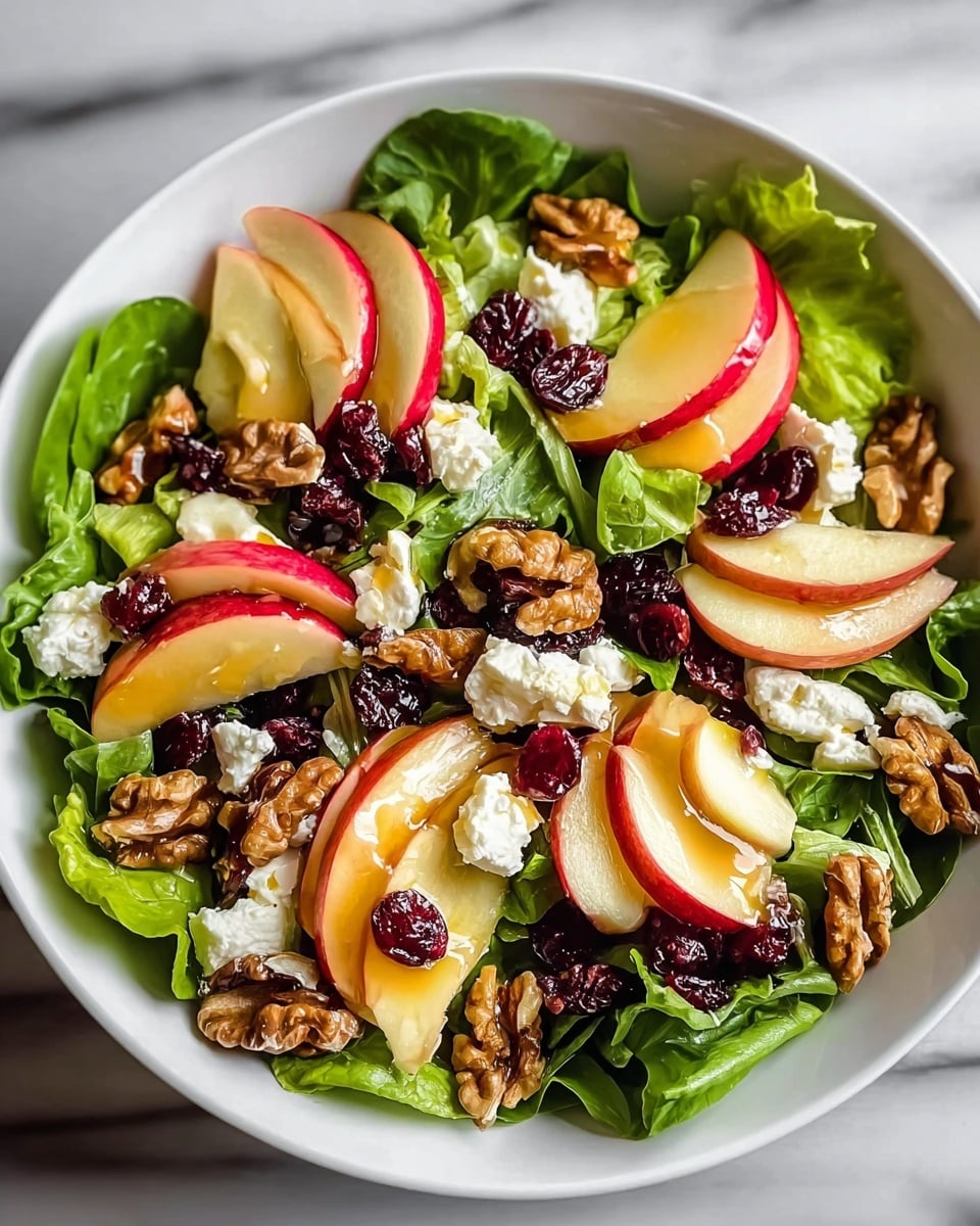 A white bowl filled with a fresh salad consisting of a first layer of leafy green lettuce. On top of the greens, there are thin slices of red apple arranged in a scattered manner, some pieces showing the red skin and white flesh. Walnuts are spread generously over the apple slices, adding a rough texture and a warm brown color. Small dollops of white goat cheese are interspersed among the walnuts and apples. Dark red dried cranberries are scattered across the salad, adding pops of color. A shiny light honey or dressing is drizzled lightly over the top, giving the ingredients a slight glossy look. The bowl rests on a white marbled surface. photo taken with an iphone --ar 4:5 --v 7