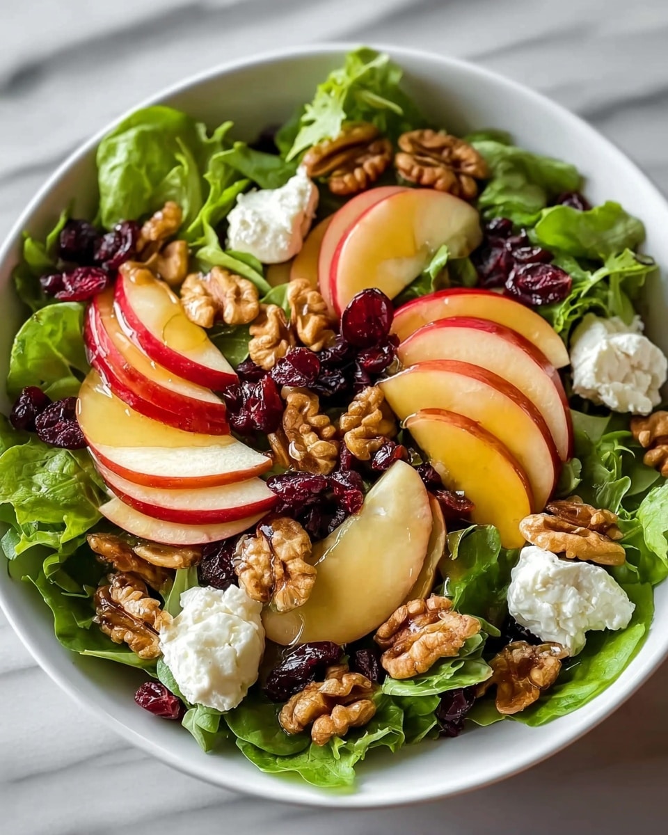 A fresh salad is shown in a white bowl on a white marbled surface, with a base layer of bright green leafy lettuce. On top, there are thin slices of red apple with a smooth texture, scattered evenly. Next, a middle layer of walnut halves adds a rich brown color and a rough texture. Small dried cranberries, dark red and wrinkled, are spread throughout the salad for a pop of color. Clusters of soft white goat cheese are placed around the bowl, adding contrast. The salad is finished with a light drizzle of honey, giving a shiny glaze over some apple slices and walnuts. photo taken with an iphone --ar 4:5 --v 7