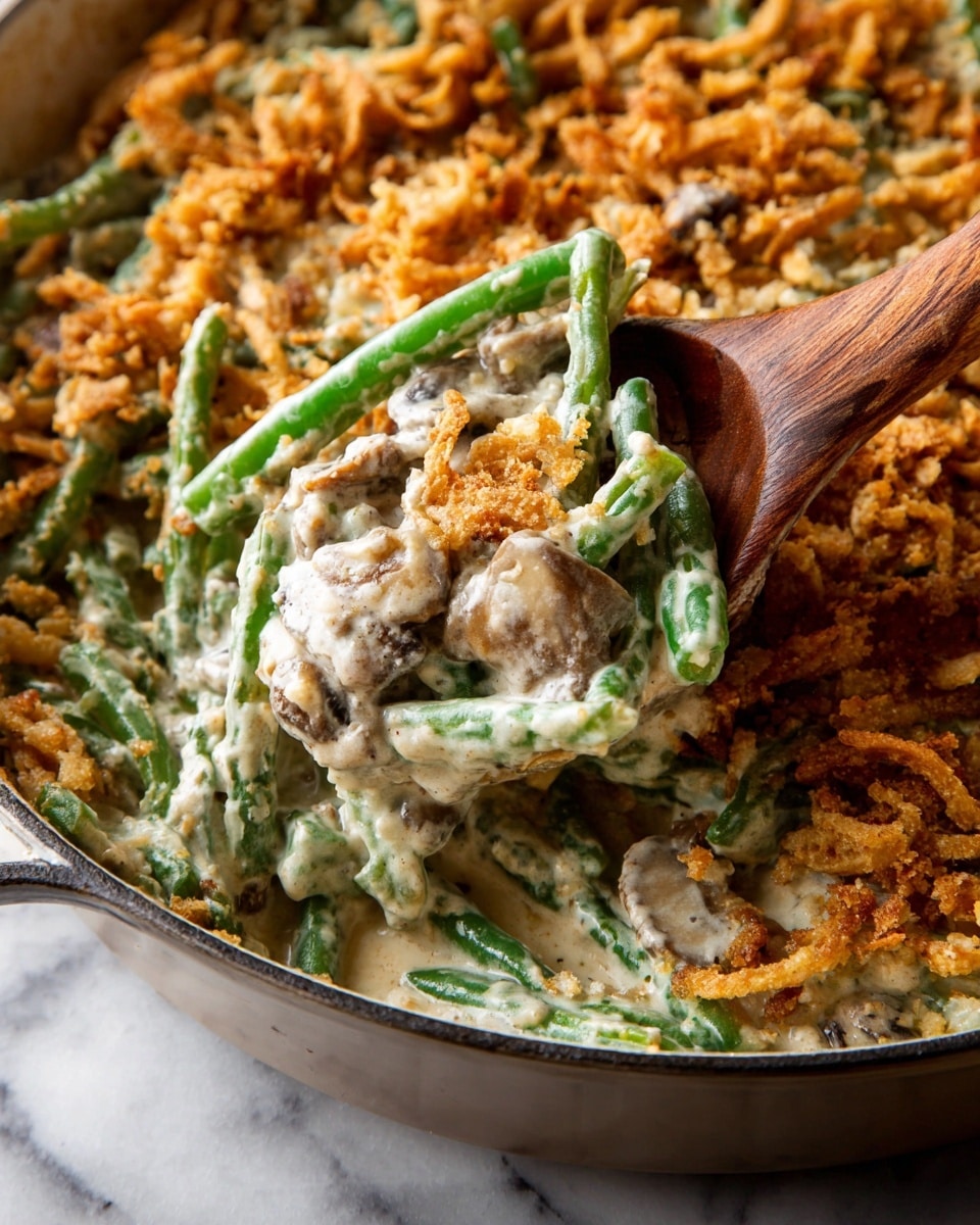 This image shows a close view of a green bean casserole in a round baking dish. The dish has three main layers: vibrant green beans coated in a creamy white sauce with small mushroom pieces mixed in, a middle layer of thick creamy sauce blending with the beans, and a top layer of golden brown crispy fried onion crumbs that add texture around the edges. A wooden spoon lifts a portion from the center, revealing the soft and creamy inside against the crunchy topping. The dish sits on a white marbled surface photo taken with an iphone --ar 4:5 --v 7