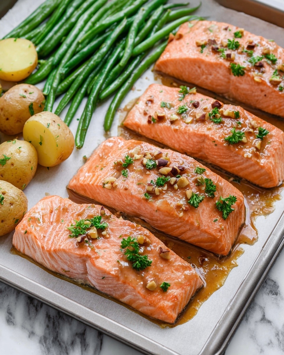 The image shows four pieces of cooked salmon placed in a row on a baking tray over white parchment paper with a light drizzle of sauce and small bits of nuts on top. Each salmon fillet has a smooth, pink-orange color with a moist texture, and a few small green parsley leaves are gently placed on each piece. Surrounding the salmon on the tray, there are some green beans arranged neatly on one side, showing a fresh and glossy dark green color, and halved small potatoes with a yellow interior and light brown, textured skin lying near the top left corner. The tray sits on a white marbled surface. Photo taken with an iphone --ar 4:5 --v 7