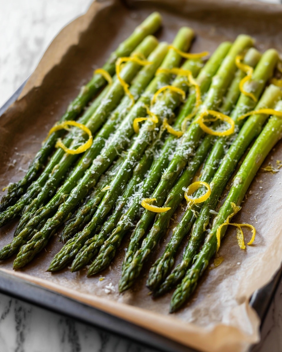A tray lined with parchment paper holds a single layer of bright green asparagus spears arranged side by side from the bottom left to the top right. Each spear is glossy, showing slight char marks near the tips, which are darker green with a delicate, textured appearance. Thin, curly yellow strips of lemon zest and a fine sprinkling of grated white cheese rest on top of the asparagus, adding contrast in color and texture. The tray sits on a surface with a white marbled texture visible in the blurred background. photo taken with an iphone --ar 4:5 --v 7