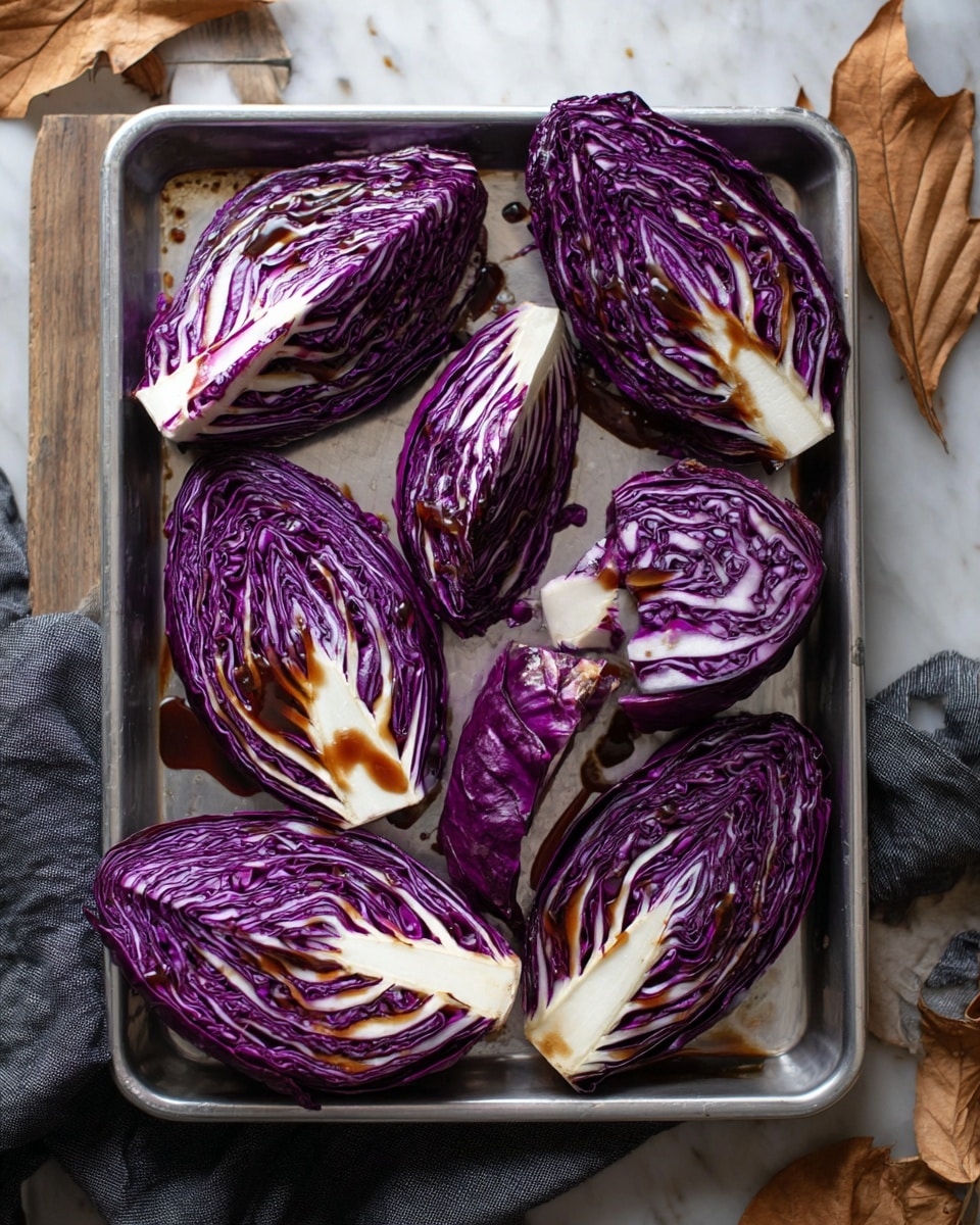 The image shows a silver baking tray filled with eight wedges of fresh purple cabbage. Each cabbage wedge has deep purple layers mixed with creamy white veins and stems. A dark brown sauce is drizzled unevenly over the cabbage wedges, adding gloss and contrast to the matte cabbage texture. The tray sits on a white marbled surface, and around it, there are a few dry brown leaves and part of a dark grey cloth. The lighting highlights the crisp texture of the cabbage leaves and the shine of the sauce. photo taken with an iphone --ar 4:5 --v 7