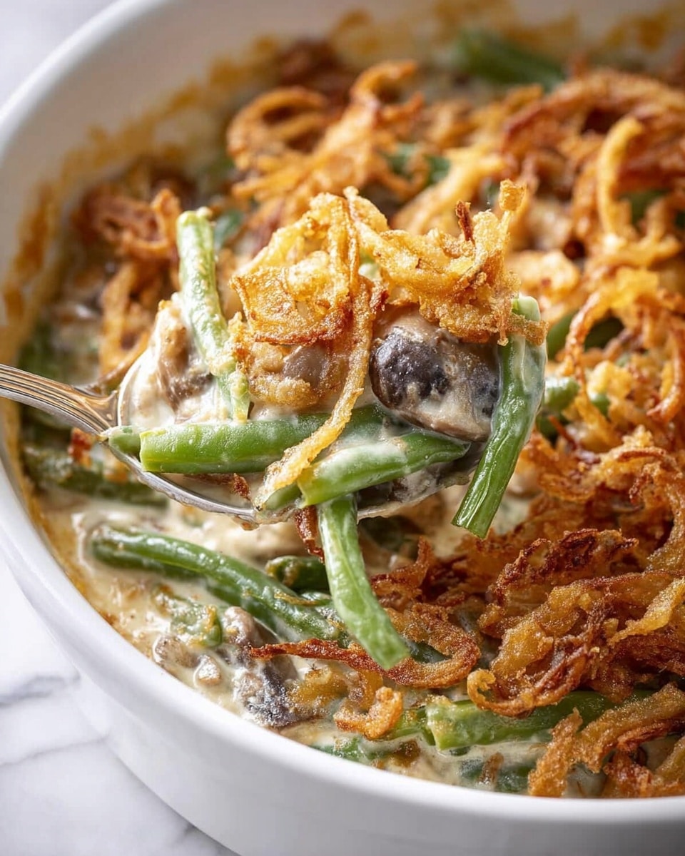 A close-up view of a white bowl filled with creamy green bean casserole, showing a mix of bright green beans and tender mushroom pieces coated in a smooth, light tan sauce. The top layer is covered in a thick, even spread of crispy, golden-brown fried onions with some pieces curling and overlapping, creating a crunchy texture contrast. A silver spoon scoops into the casserole, lifting the creamy veggie mixture and breaking through the crunchy onion layer. The background surface is a white marbled texture. photo taken with an iphone --ar 4:5 --v 7