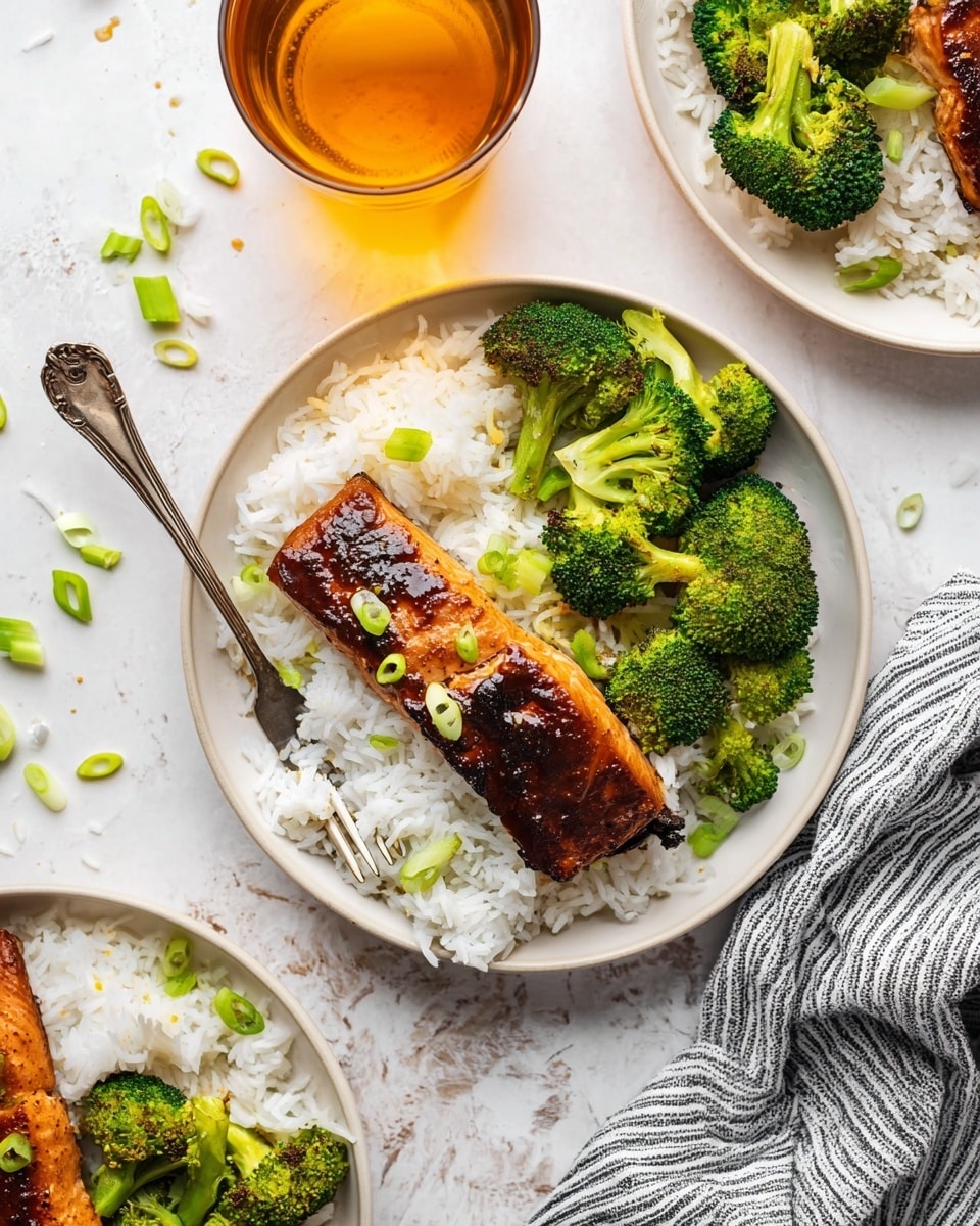A white round plate holds a meal with three layers: at the bottom is a bed of white rice with a slightly sticky texture, layered with a dark brown glazed grilled salmon fillet centered on top, garnished with small green sliced scallions. On one side of the salmon, bright green steamed broccoli florets form the third layer, showing a fresh, firm texture. A silver fork rests on the left edge of the plate, against a white marbled textured surface. Nearby, a glass of iced amber tea and another white round plate with the same meal are partly visible, with scattered green scallion slices around. A folded gray-striped cloth adds a cozy touch near the bottom right corner. photo taken with an iphone --ar 4:5 --v 7