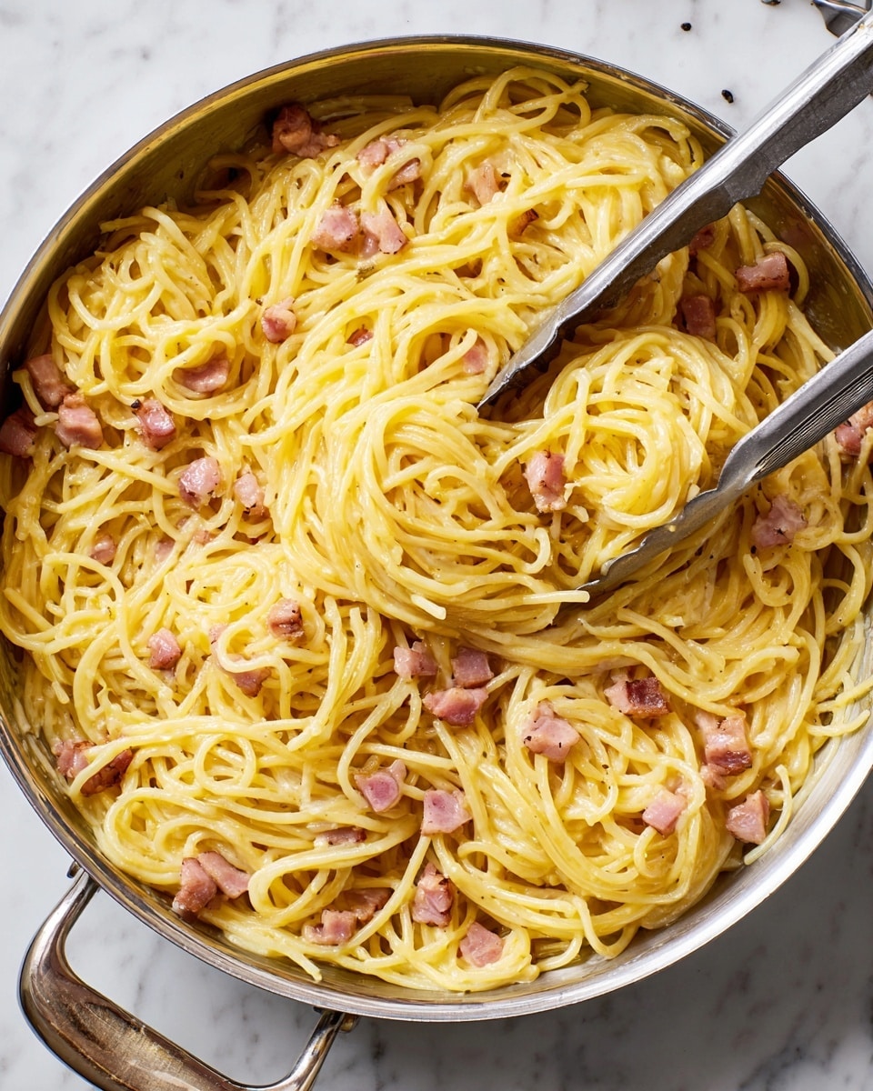 A top view of creamy spaghetti carbonara in a metal pan with a shiny handle, showing one layer of smooth, glossy yellow pasta strands mixed with small pieces of cooked bacon that have a pink and brown color. The pasta looks soft and coated evenly with sauce, while metal tongs are placed inside the pan holding a small bundle of noodles. The background is a white marbled texture. photo taken with an iphone --ar 4:5 --v 7